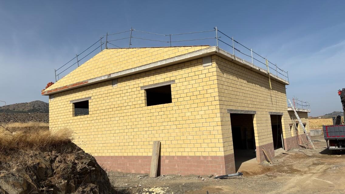 Construcción de edificio técnico con ladrillo caravista en zona industrial, obra en curso con estructura completa.
